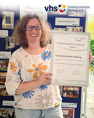 Kerstin Meißner, Leitung der vhs Olching, hält das Zertifikat hoch.